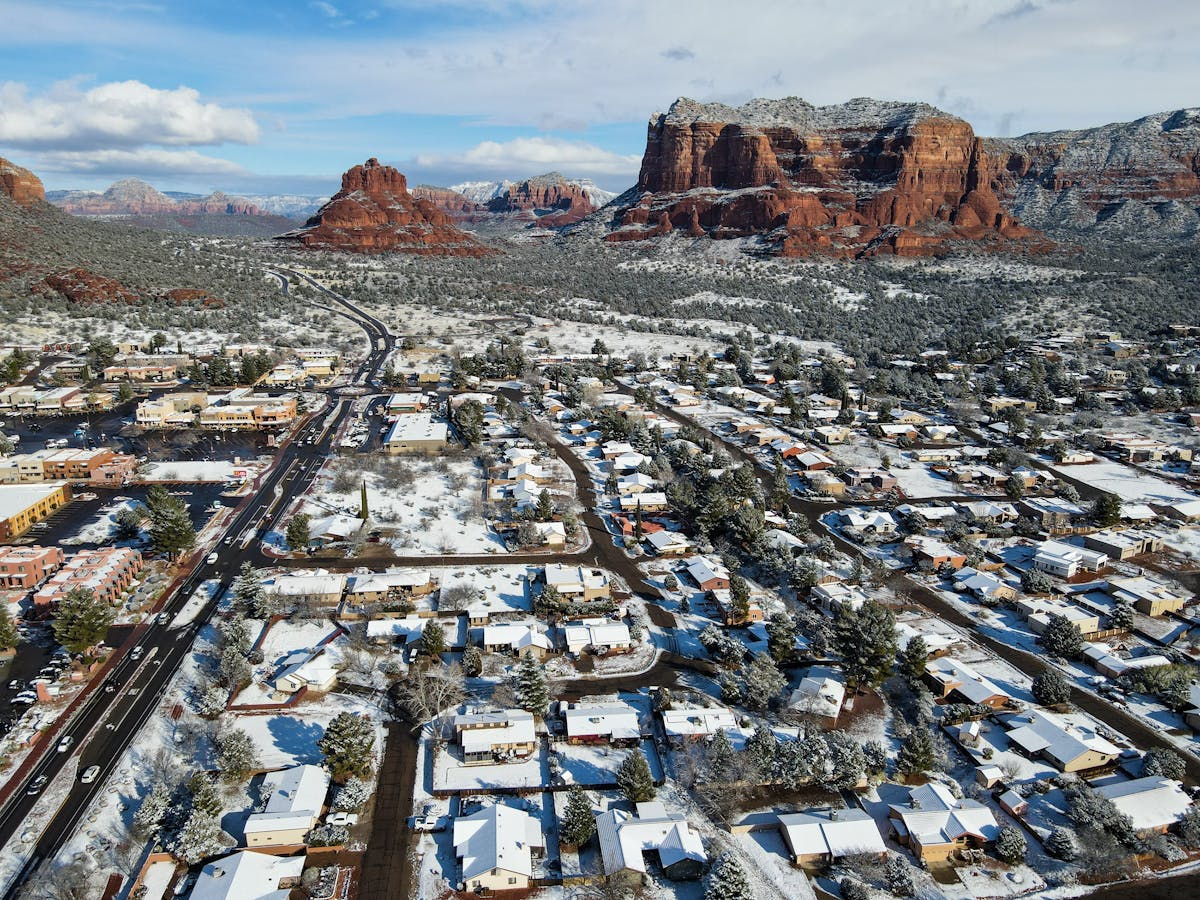 A breathtaking aerial view of Sedona, Arizona, showcasing snow-covered houses and iconic red rock formations.