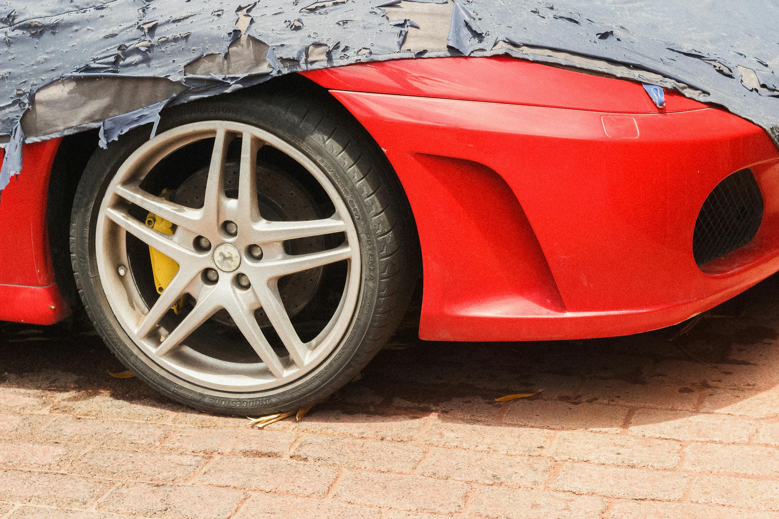 Close-up of a red sports car tire, partially covered with a tarp outdoors.