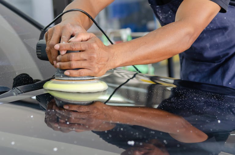 Detailed view of a worker's hands polishing a car's hood using a buffer in an auto workshop. ppf lifespan arizona