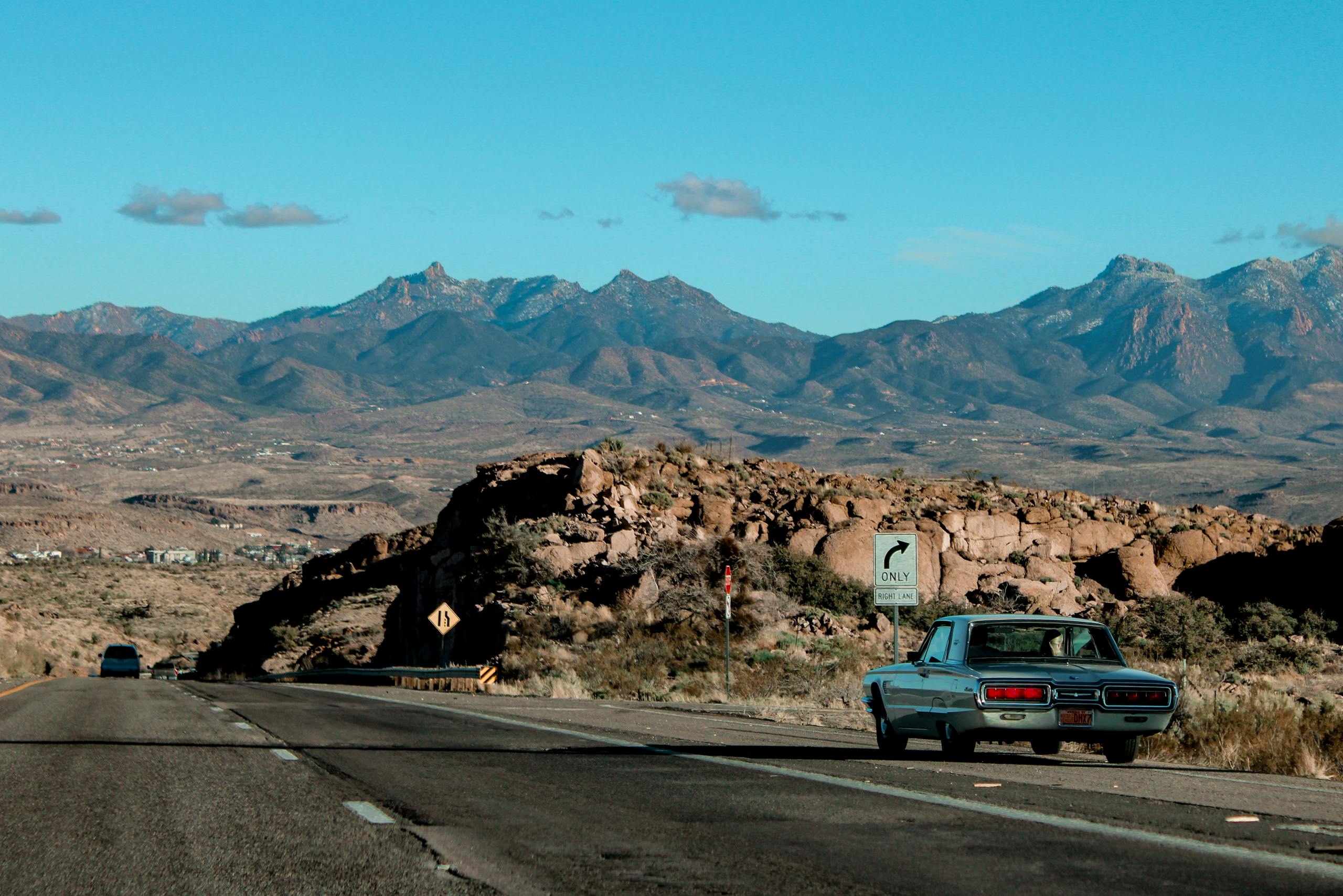 Vintage car travels along a scenic highway in the Arizona desert with majestic mountain views.